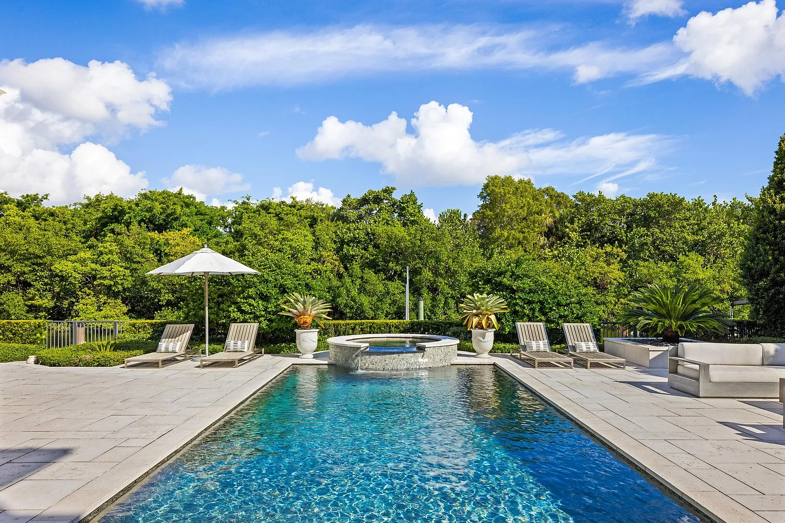 The backyard centers around a rectangular pool and raised spa surrounded by expansive stone decking and lounge chairs.