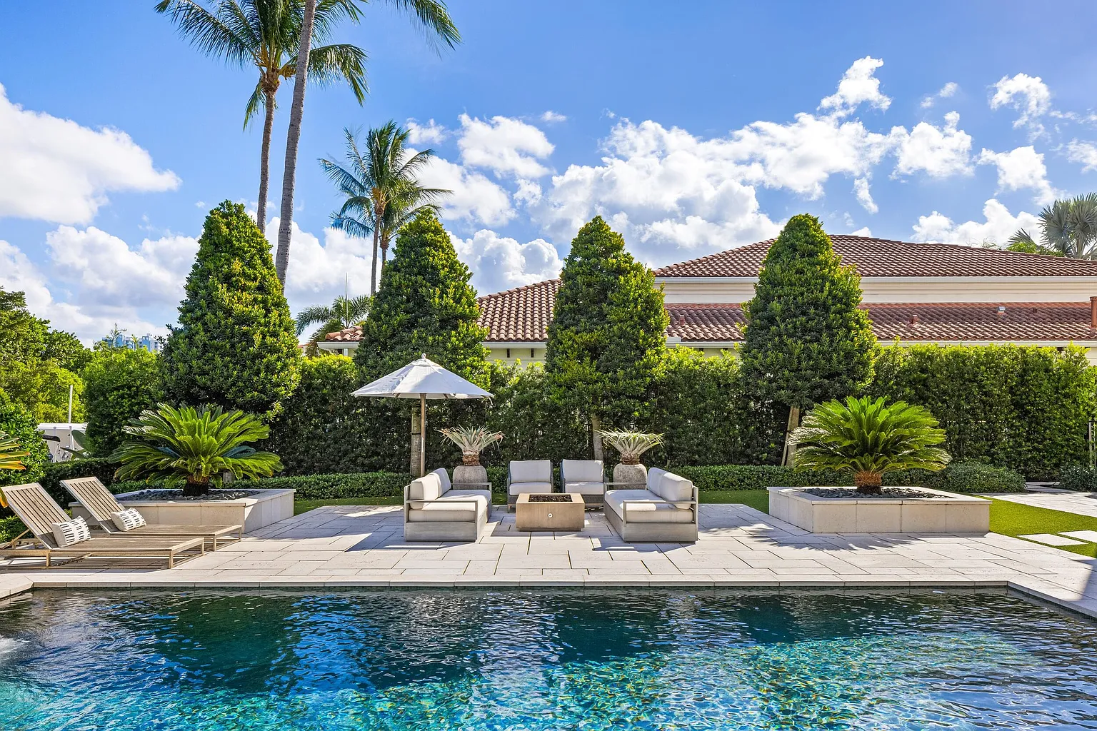 Across from the pool, a dedicated seating area is arranged around a firepit, creating a natural gathering place after sunset.
