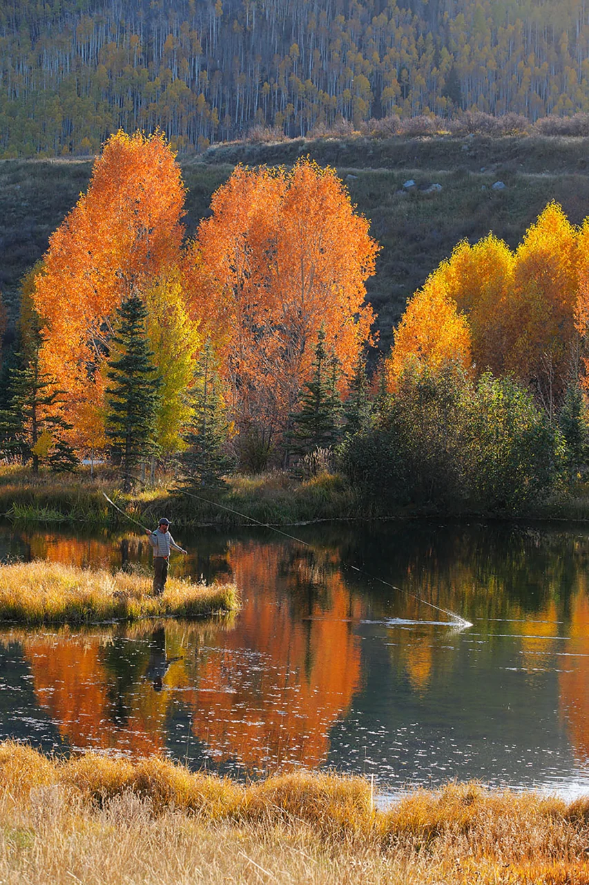 Man fishing in a pond surrounded by Fall trees.