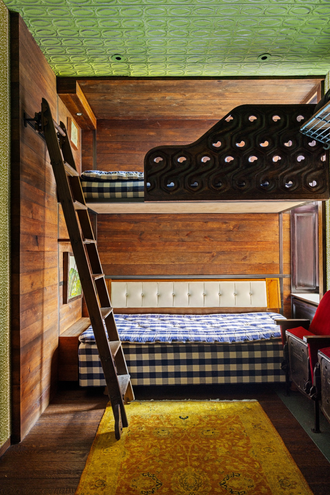 A built-in ladder leads to the upper bunk beneath the room's green, patterned ceiling and cabin-inspired design.