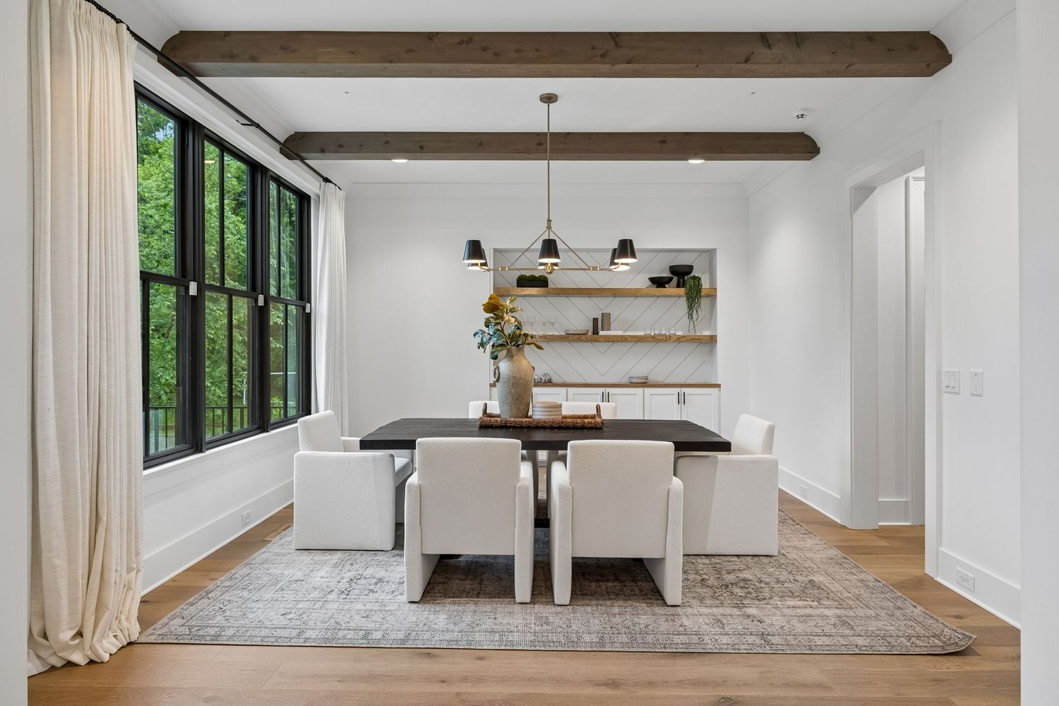 At the center sits a dark wood dining table surrounded by white chairs.