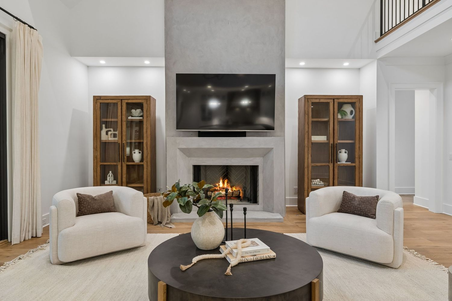 Oversized seating is arranged around a round coffee table, facing a floor-to-ceiling fireplace finished in a smooth plaster that extends nearly two stories high.