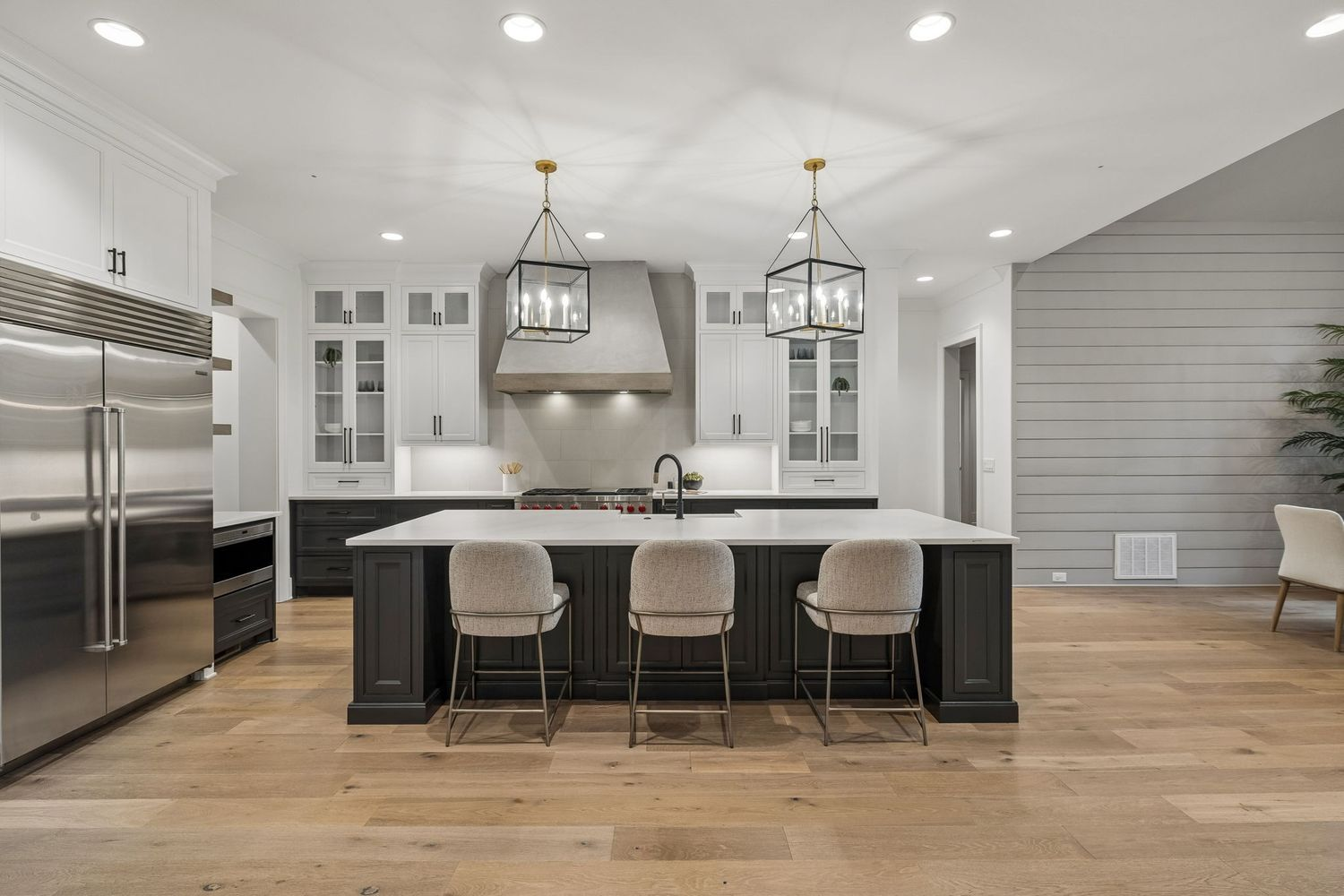 The kitchen is centered around an island finished with a waterfall-style countertop, while white upper cabinetry surrounds a custom vent hood and professional-grade Wolf gas range. 