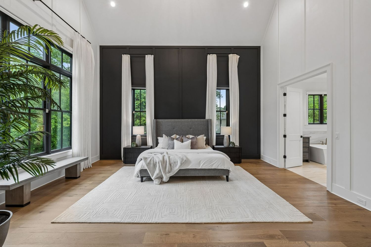 Located on the main level, the primary suite is designed as a spacious private wing with soaring ceilings, oversized windows, and a dramatic floor-to-ceiling accent wall behind the bed. 