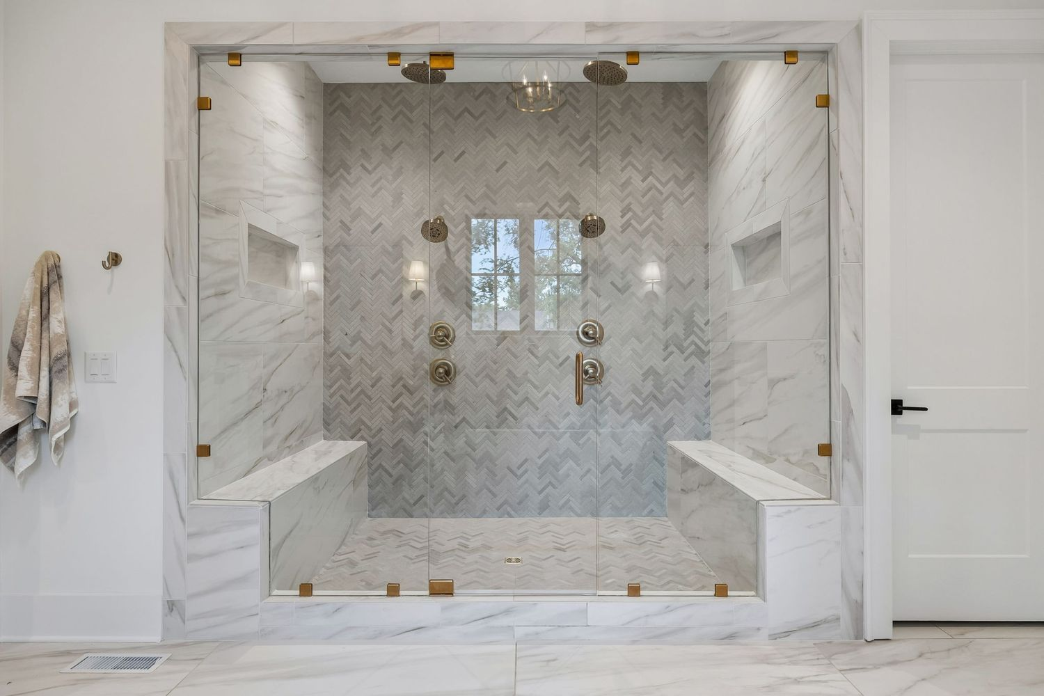 A separate walk-in shower occupies its own space across the room, featuring full-height glass walls, dual rainfall showerheads, built-in bench seating on both sides, and recessed storage niches.