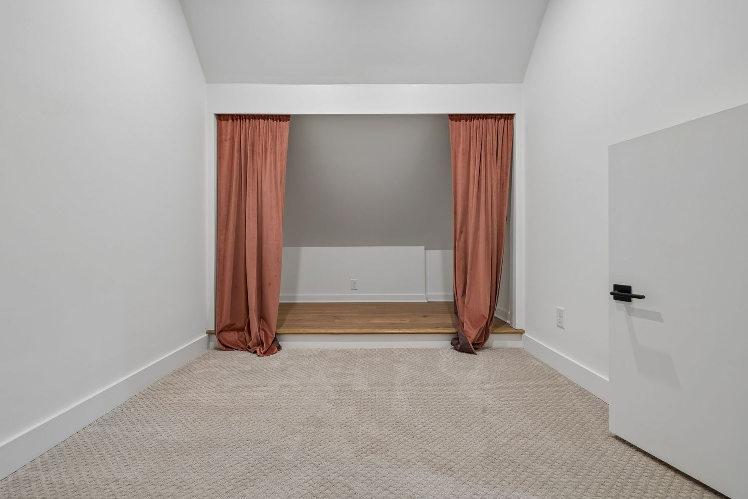 Soft carpeting creates a comfortable surface for younger children, while a raised alcove framed by floor-to-ceiling drapery offers a built-in stage, reading nook, or imaginative play area.