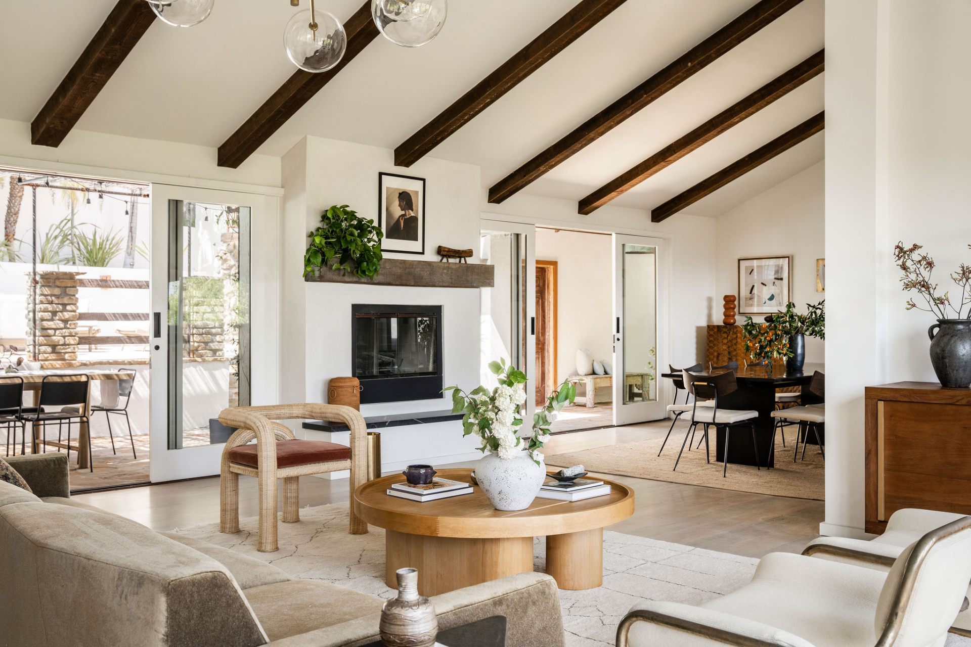 Vaulted ceilings lined with exposed dark wood beams add scale overhead, while a contemporary fireplace anchors one side of the room.