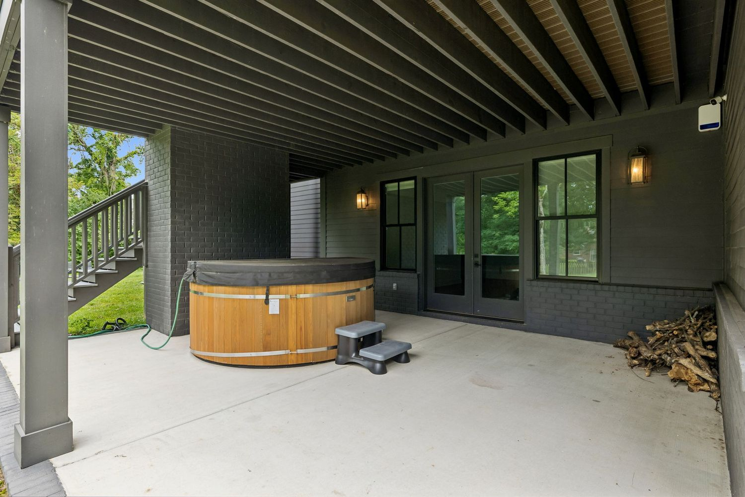 Beneath the screened porch, a covered lower-level patio creates another outdoor gathering space, which features a cedar hot tub positioned beside the home's dark-painted brick exterior.