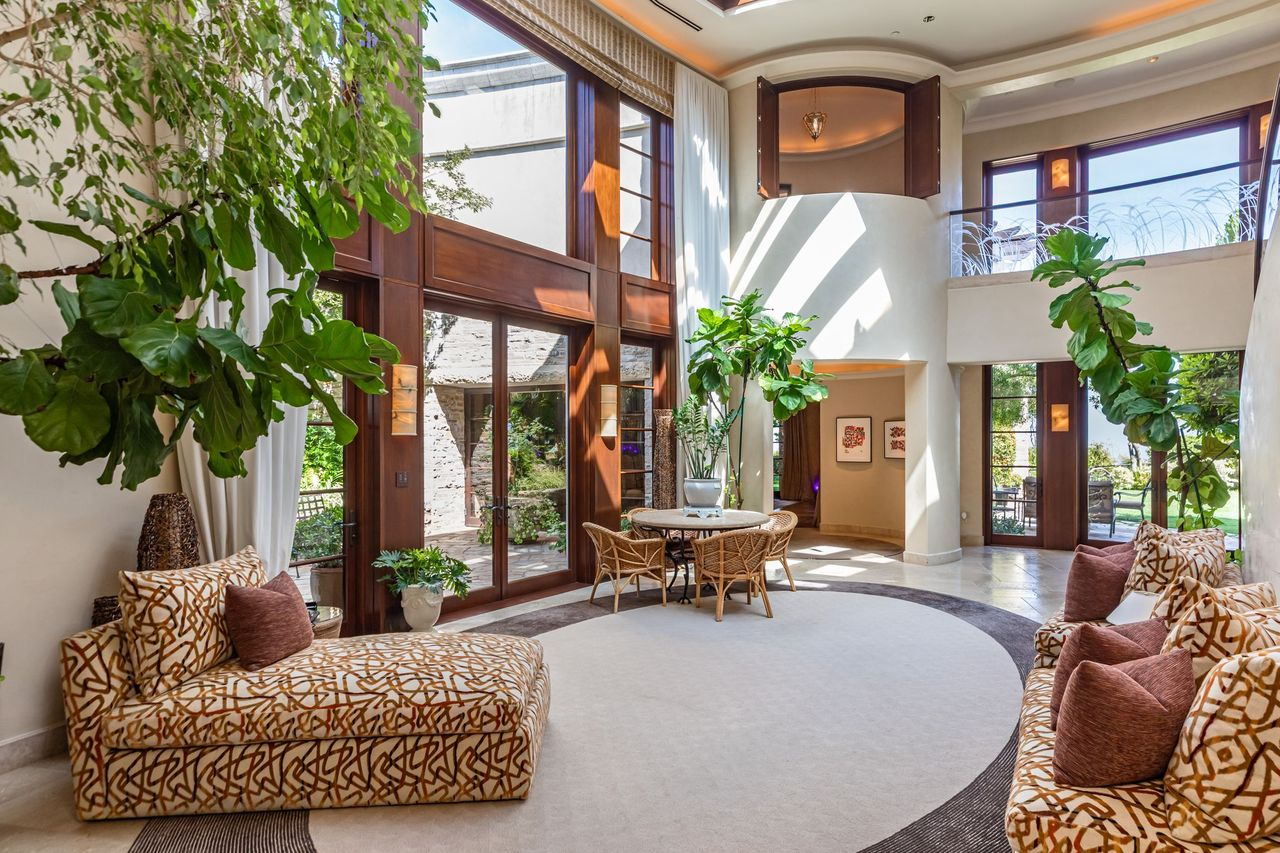 Two-story ceilings rise above a circular seating area, while oversized wood-framed glass doors and windows fill the space with natural light.