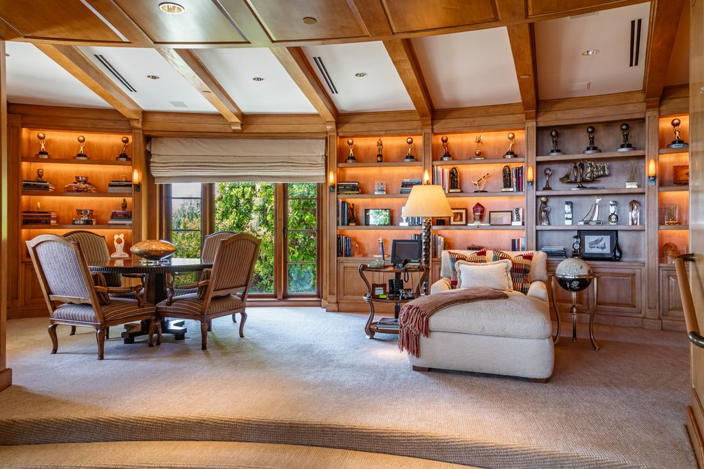 Warm wood paneling wraps the room from floor to ceiling, while built-in bookshelves showcase books, awards, sculptures, and memorabilia.