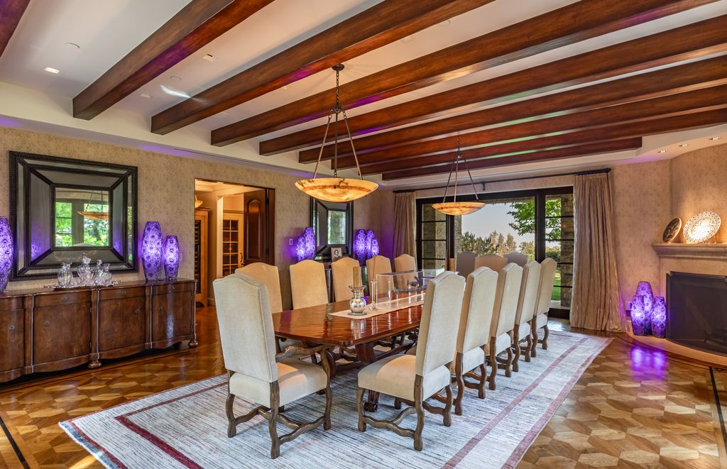 A formal dining room with exposed wood beams stretching across the ceiling above a long dining table with seating for a dozen guests.