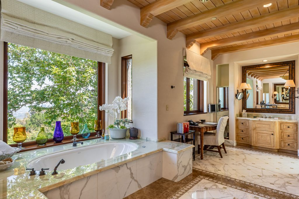The suite's bathroom is finished in marble and arranged around a large soaking tub, which sits alongside a vanity with marble countertops and custom cabinetry.