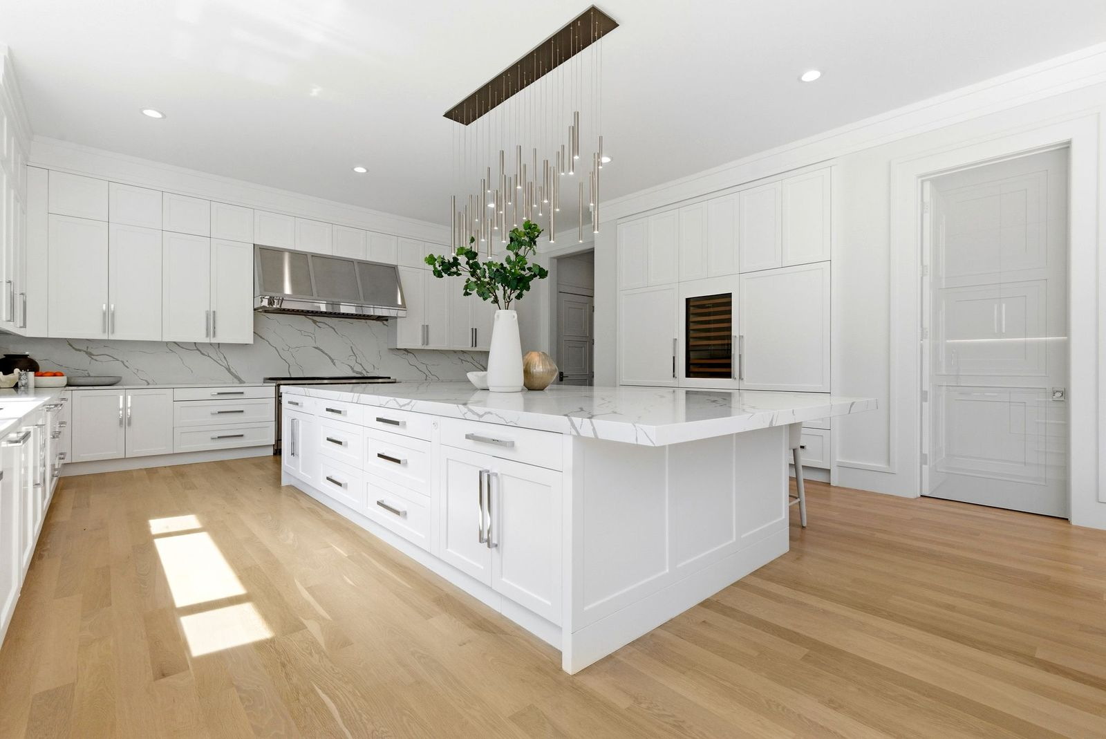 Beyond the dining area, the chef's kitchen is finished in a clean palette of white cabinetry, light oak floors, and full-height marble-look slab backsplashes.