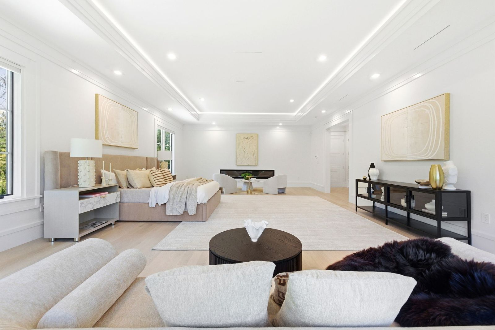 A fully upholstered bed sits in the middle of the room, while at the far end, a sitting area gathers around a linear fireplace, creating a separate space for reading or relaxing.