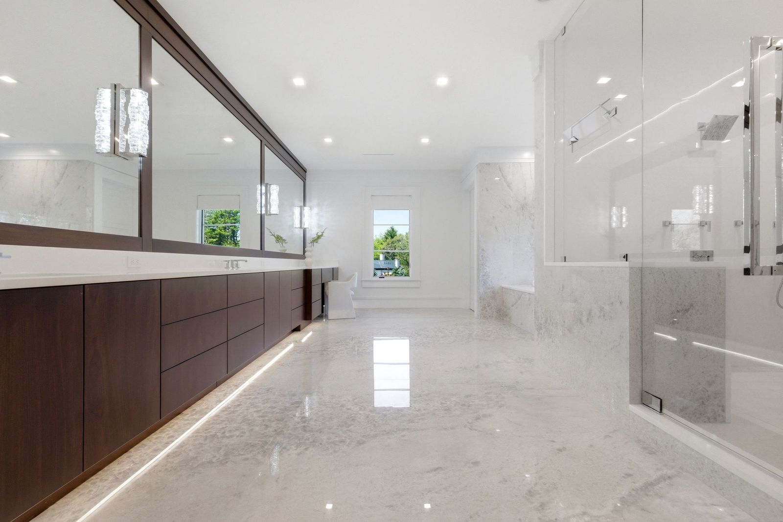 Off to one side, a long floating vanity stretches across the wall beneath oversized mirrors, offering abundant storage and counter space.