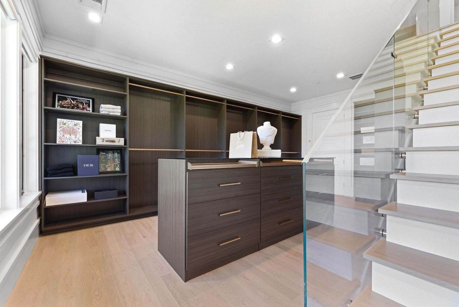A floating staircase with glass railings leads to the upper level of the closet, taking advantage of the room's vertical space.