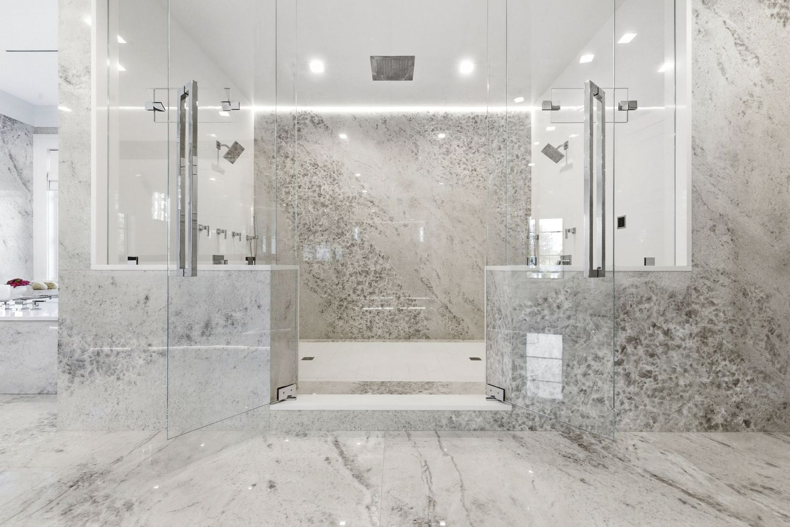 At the center of the room is a walk-through shower enclosed in glass, with marble extending across the walls and floors.
