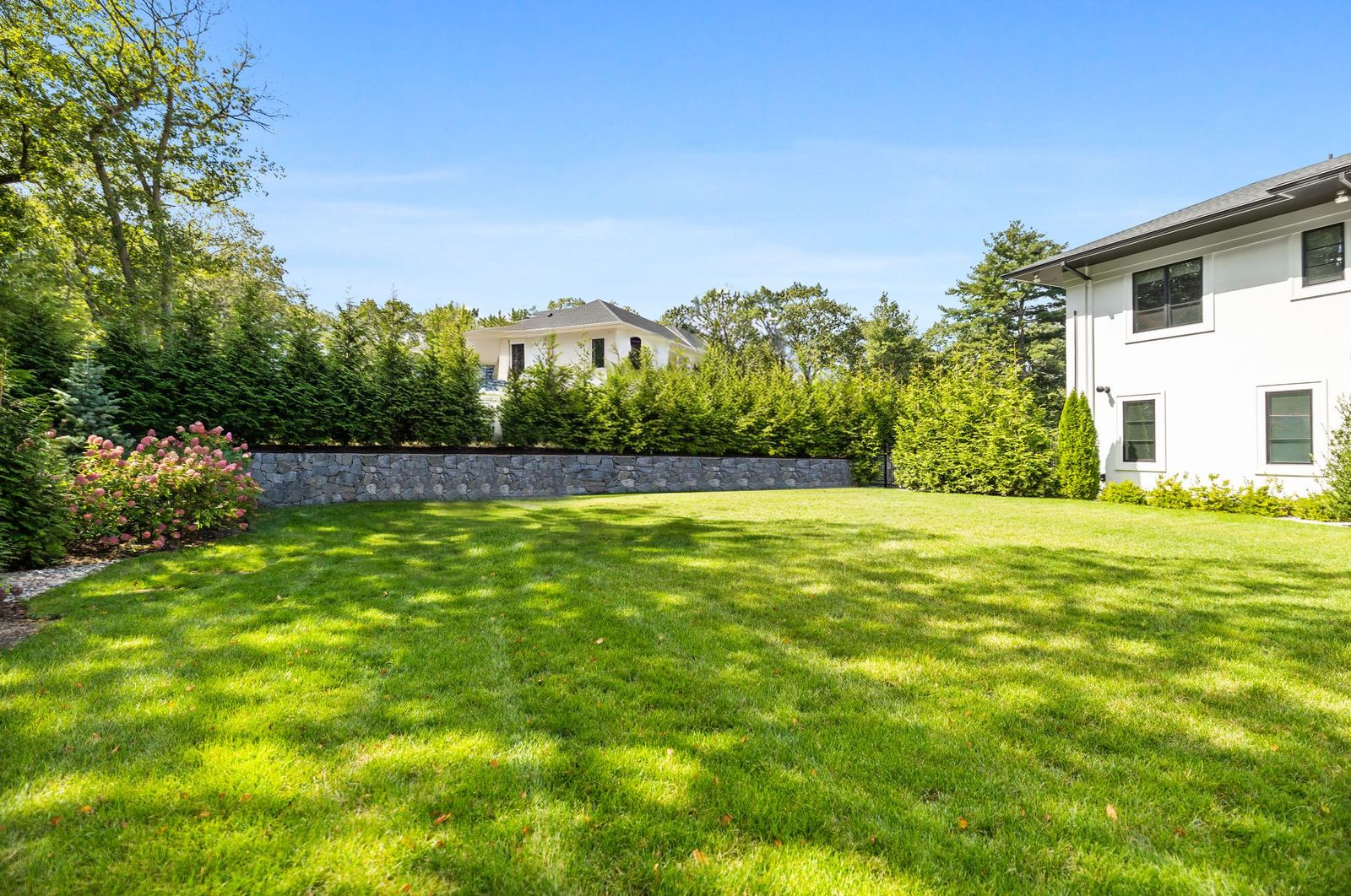 The nearly level yard extends across much of the 1.6-acre property, bordered by mature landscaping, privacy hedges, and stone retaining walls.