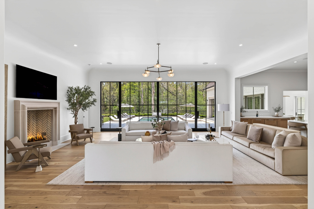 At one end of the room, a limestone fireplace with a herringbone firebox serves as the focal point, framed by lounge chairs and display cabinetry.