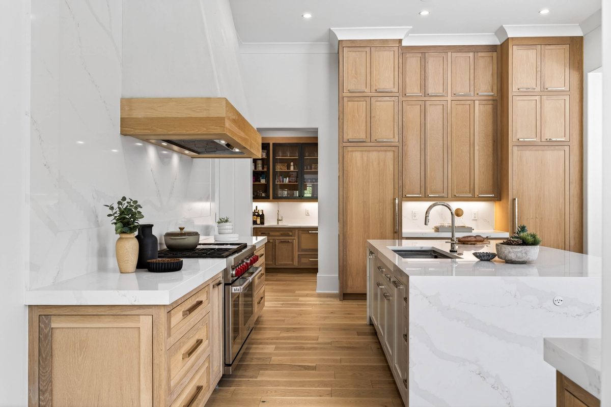 One side of the kitchen is dedicated to cooking, where premium appliances are framed by full-height slab backsplashes and a custom wood-accented vent hood.