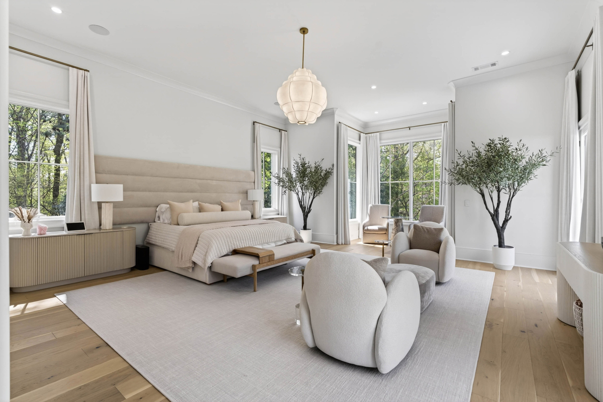 A tall upholstered headboard anchors the bed, while a grouping of curved lounge chairs creates a conversation area in front of a wall of windows overlooking the surrounding trees.