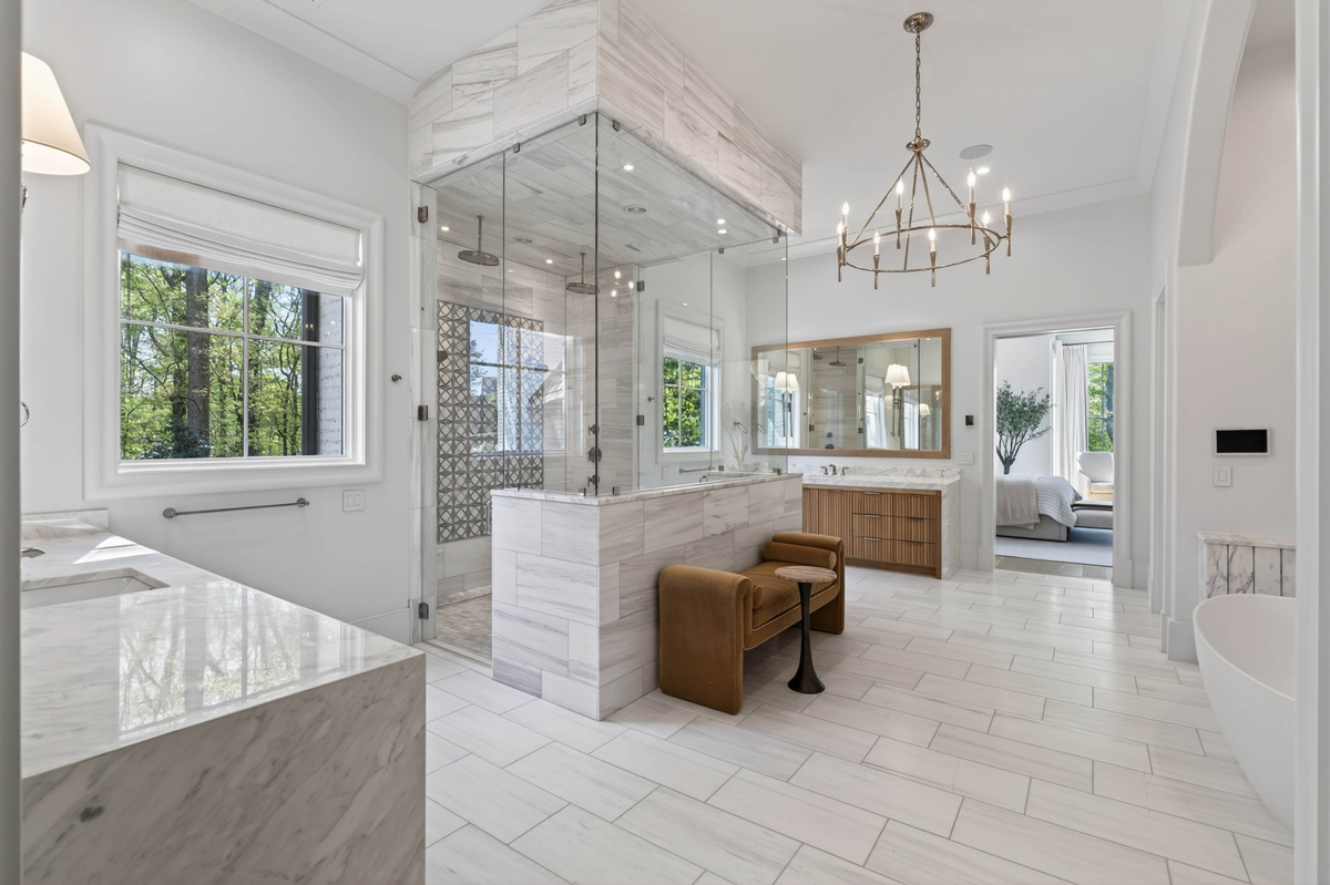 The room opens with expansive floor space, oversized fluted vanities, and a dramatic glass-enclosed shower positioned at the center of the layout.