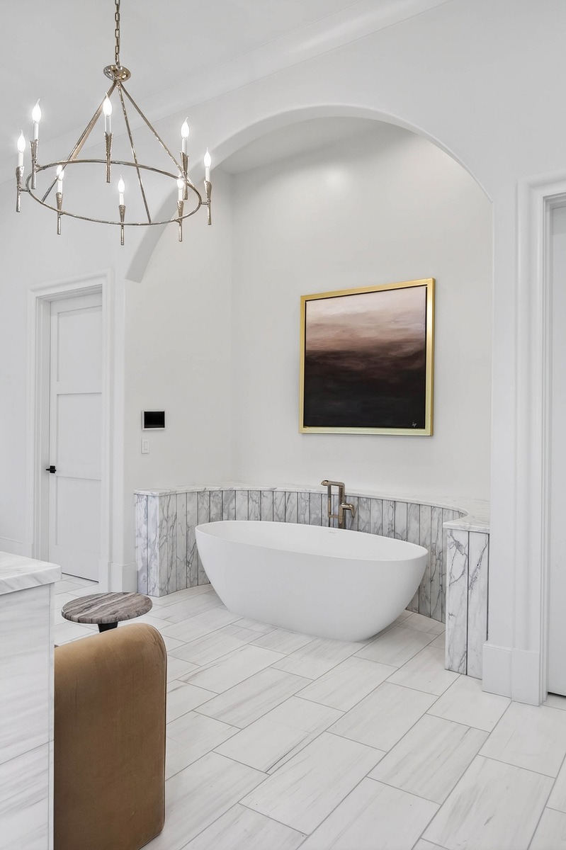 Opposite the shower sits a freestanding soaking tub tucked into an arched niche, framed by marble wainscoting and separate water closets on either side.