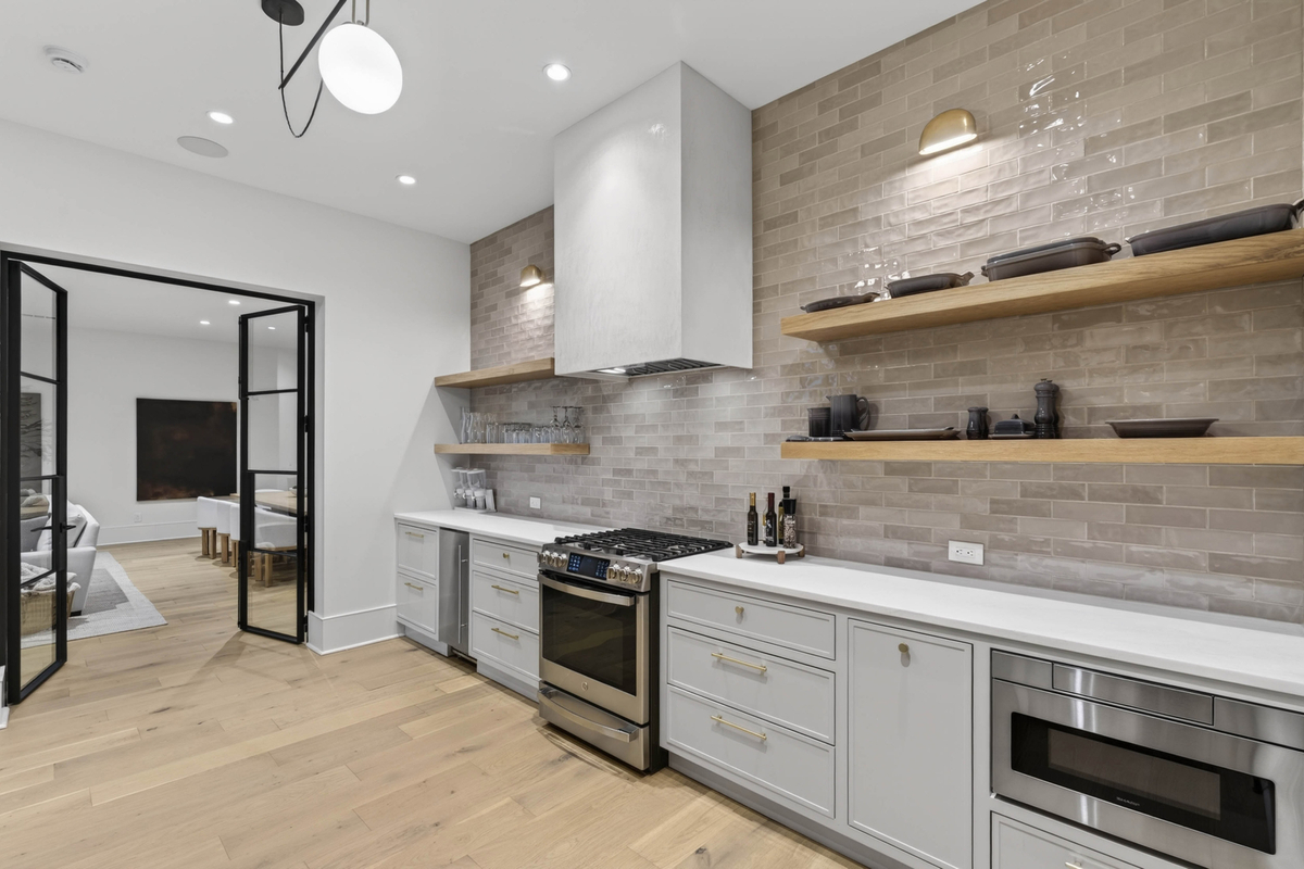 Next to the family room is a secondary full kitchen finished with stone countertops, open shelving, and a complete suite of appliances.