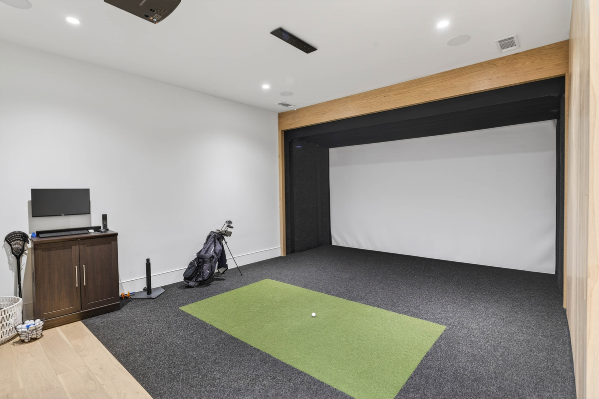 Heading into the recreational side of the complex is a golf simulator room equipped for full swings with a projection screen, impact area, and turf flooring.