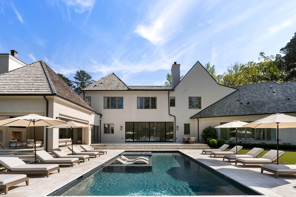 At the center of the backyard is a resort-style pool framed by expansive stone decking and rows of chaise lounges.