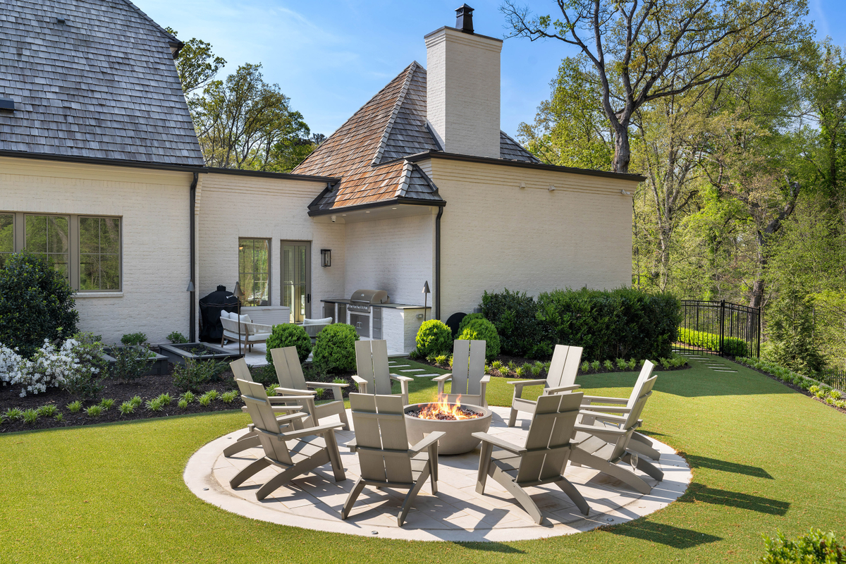 Beyond the pool, a circular firepit gathering area is surrounded by Adirondack chairs set within the lawn.