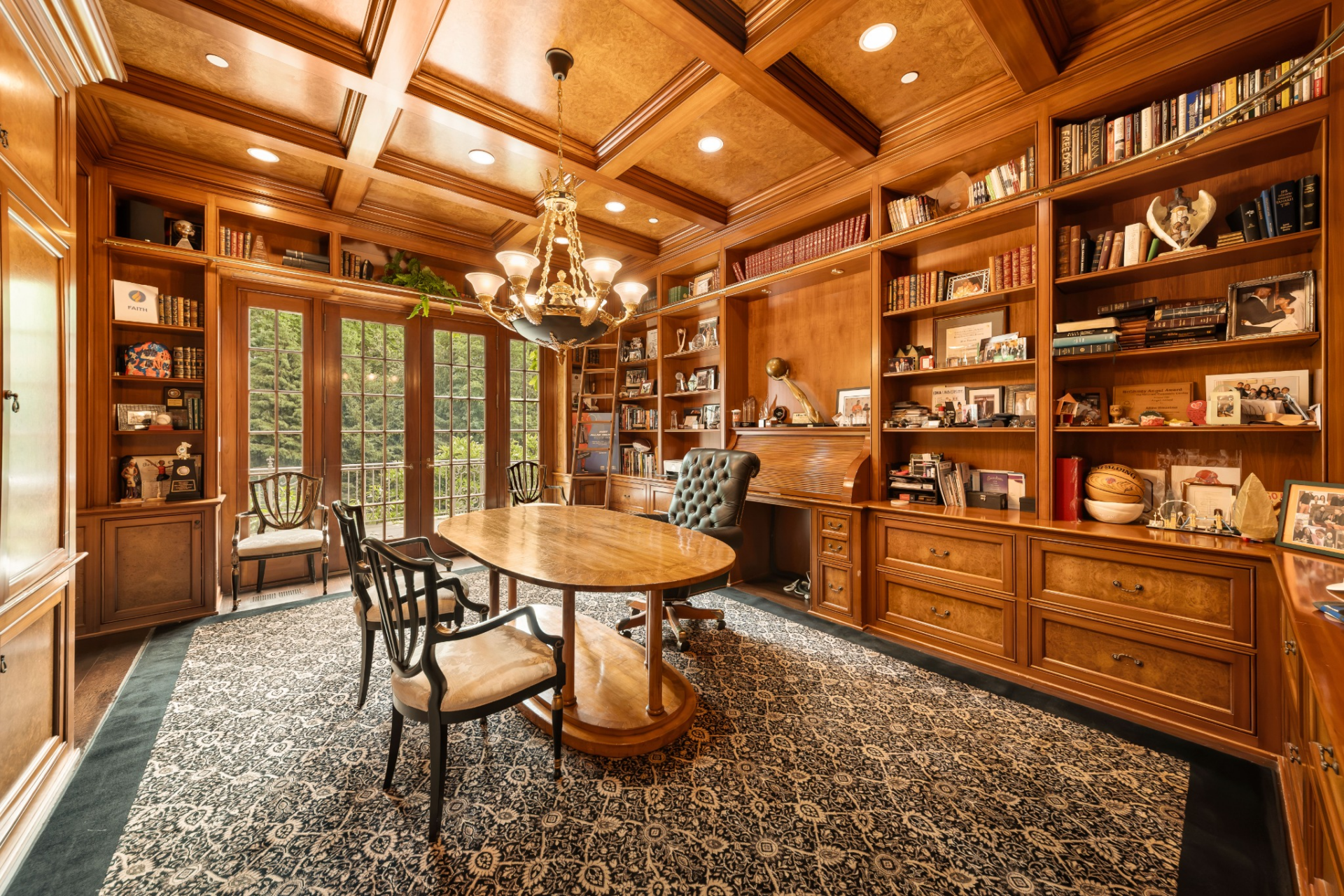 The home office is finished in richly stained wood, from the coffered ceiling overhead to the floor-to-ceiling built-in bookshelves lining the walls. 