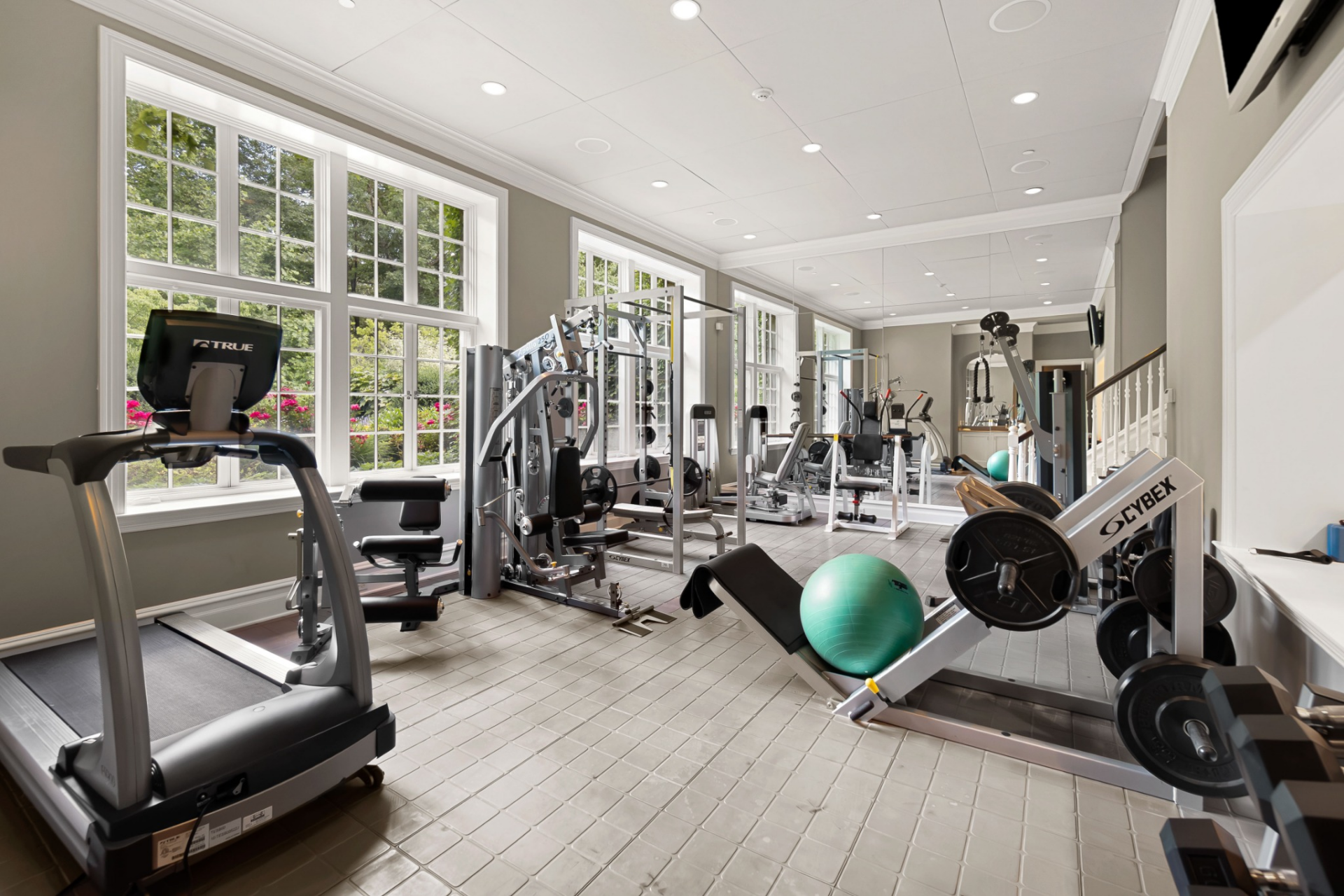 The space is equipped with cardio machines, weight-training equipment, and mirrored walls.
