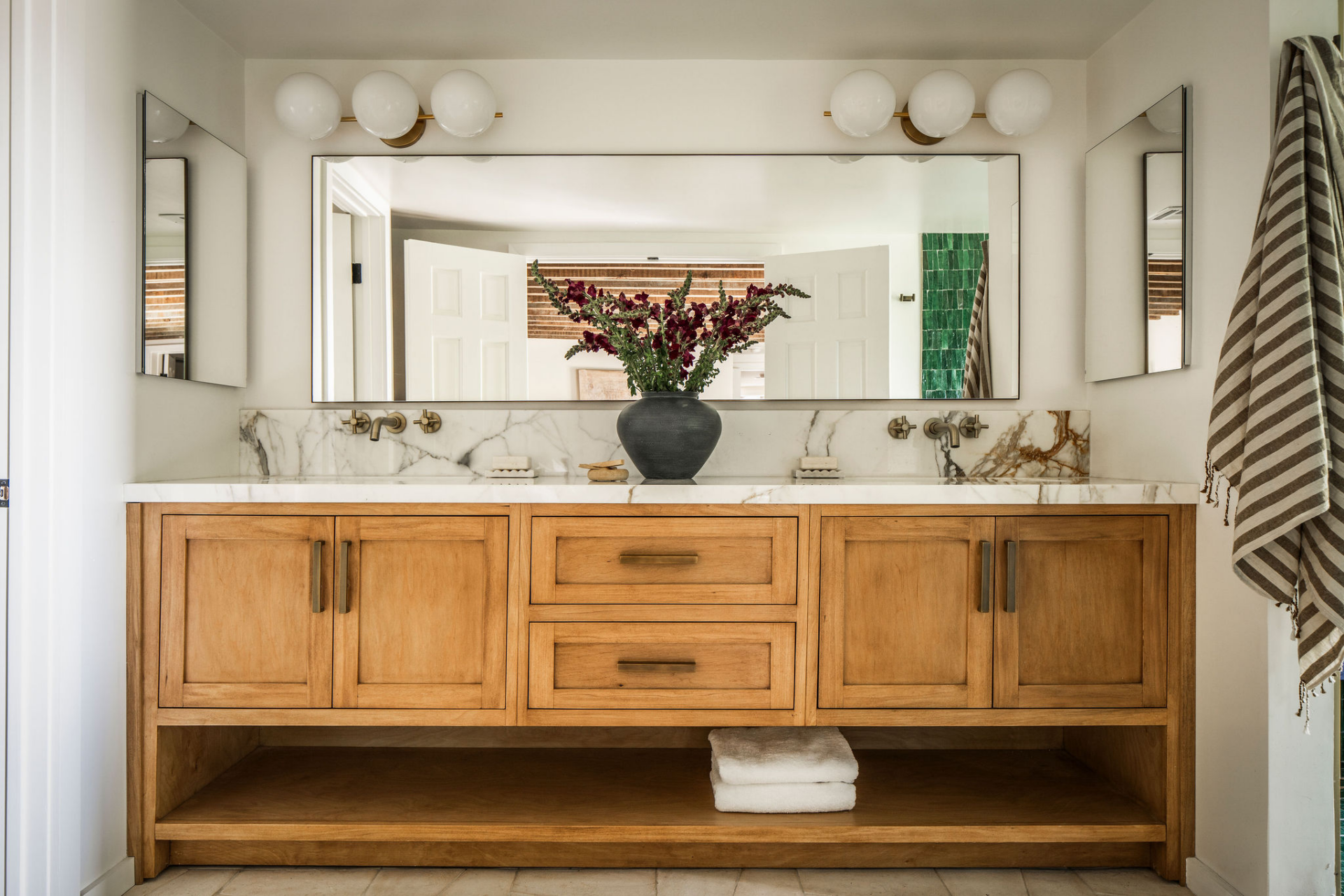 A long double vanity stretches beneath an oversized mirror, providing storage and counter space while maintaining a clean, streamlined appearance.