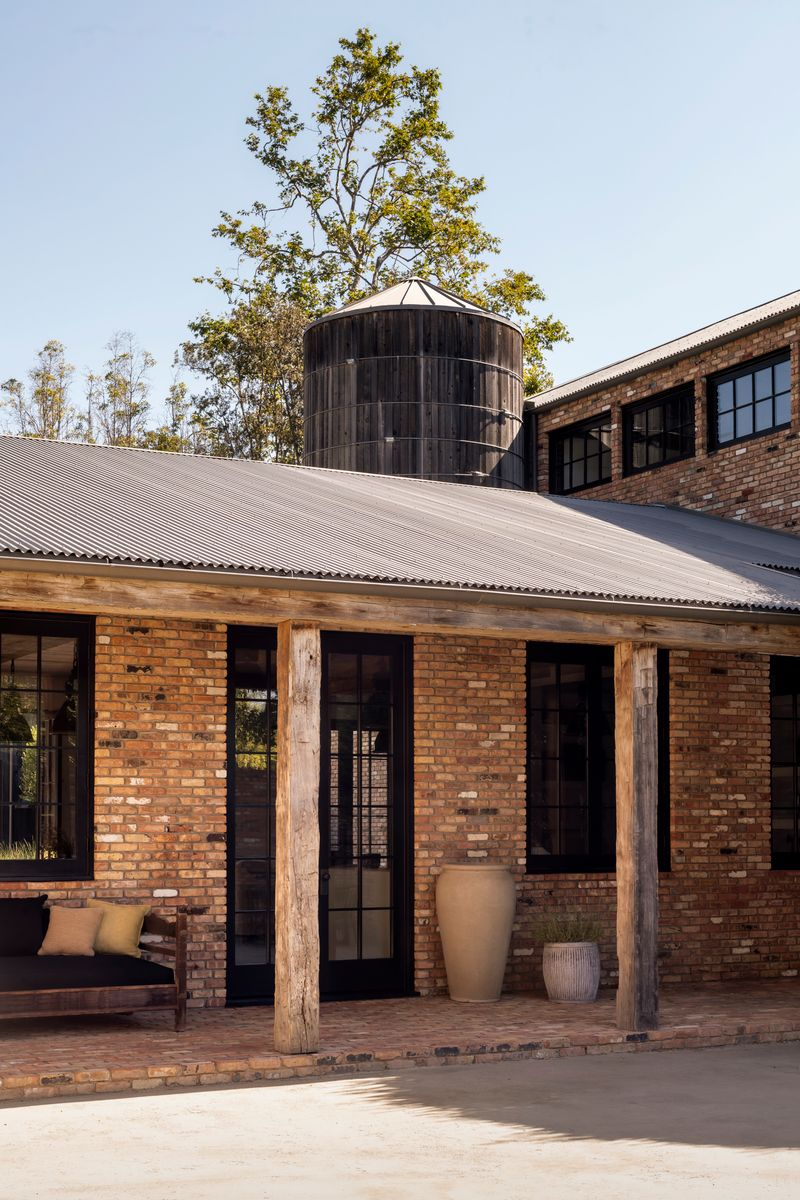 Weathered timber columns support covered porches, and steel-framed doors and windows line walls built handpicked clay bricks.
