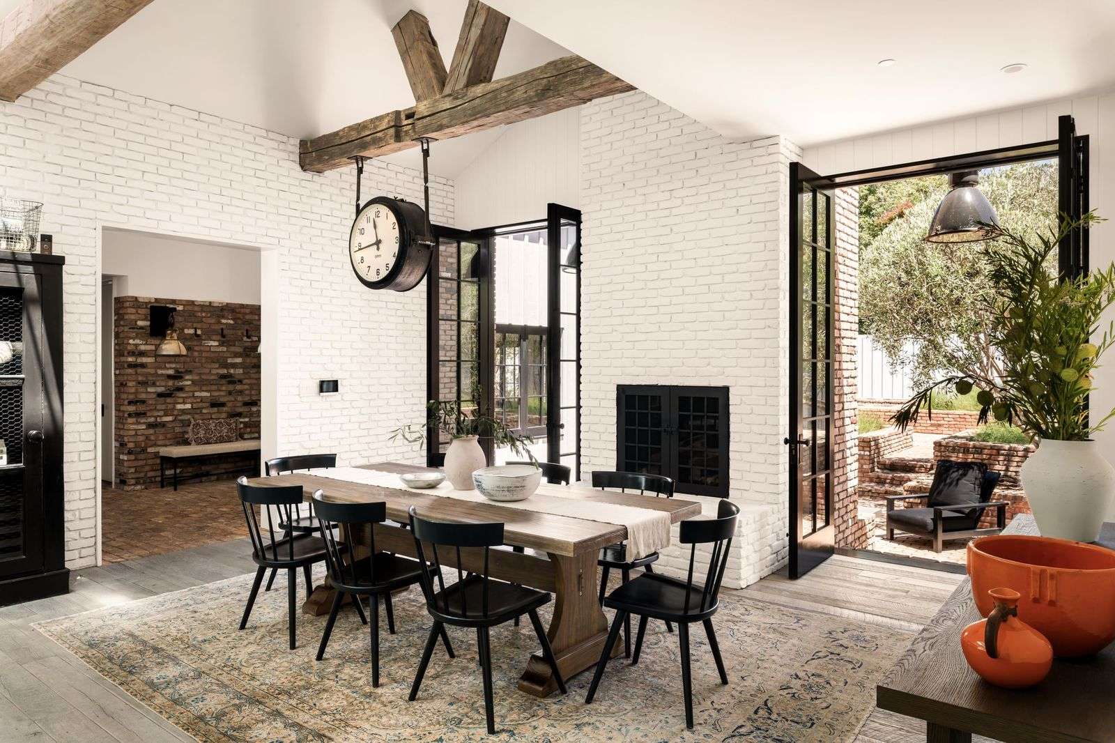 Behind the dining area, large steel-framed doors open directly to a brick courtyard, allowing the kitchen to spill naturally outdoors.