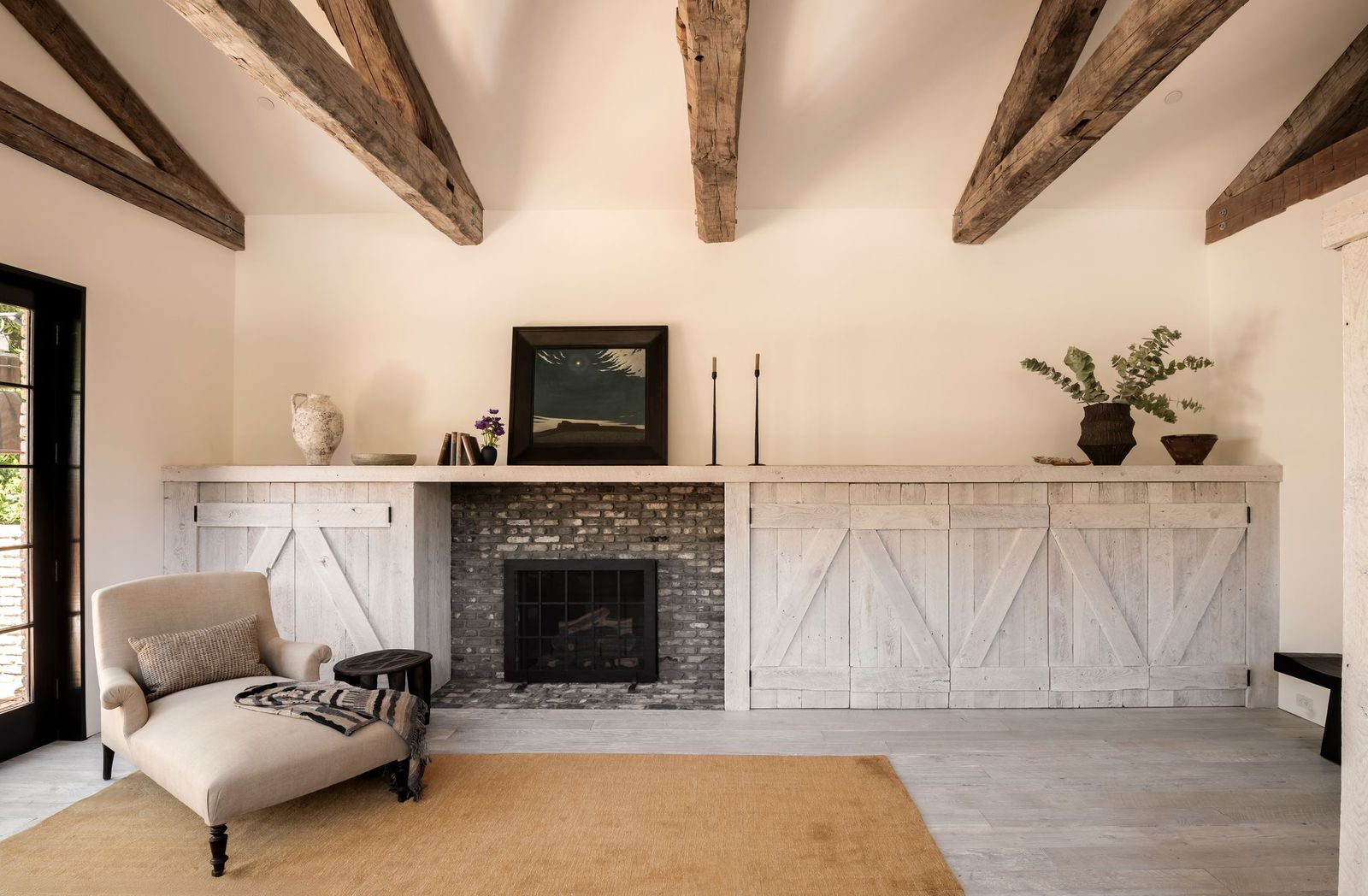 Across from the bed is a simple fireside lounge where a grey brick fireplace is placed within an entire wall of white built-in cabinetry.