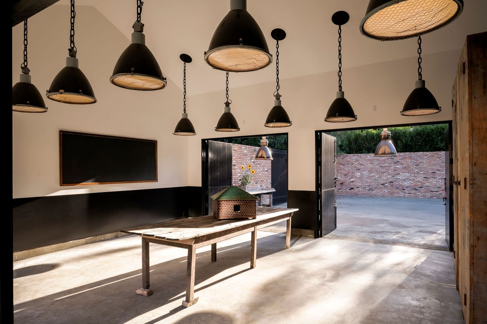 Large black industrial-style pendant lights hang from the vaulted ceiling, while oversized doors at either end open directly to the outdoor spaces on both sides of the property.