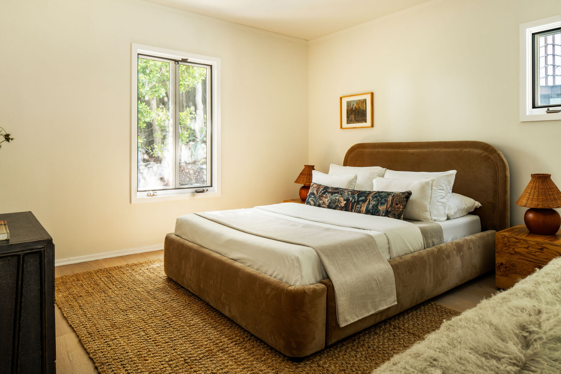 This guest room centers around a sculptural velvet-upholstered bed that introduces warmth and texture against soft neutral walls. 