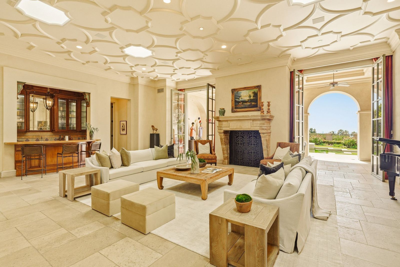 Limestone flooring continues throughout, while a carved stone fireplace sits between French doors that open directly to the surrounding gardens and covered terraces.