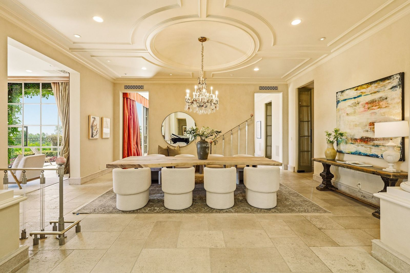 The dining room sits beneath a coffered ceiling with a crystal chandelier hanging over a long wood dining table.