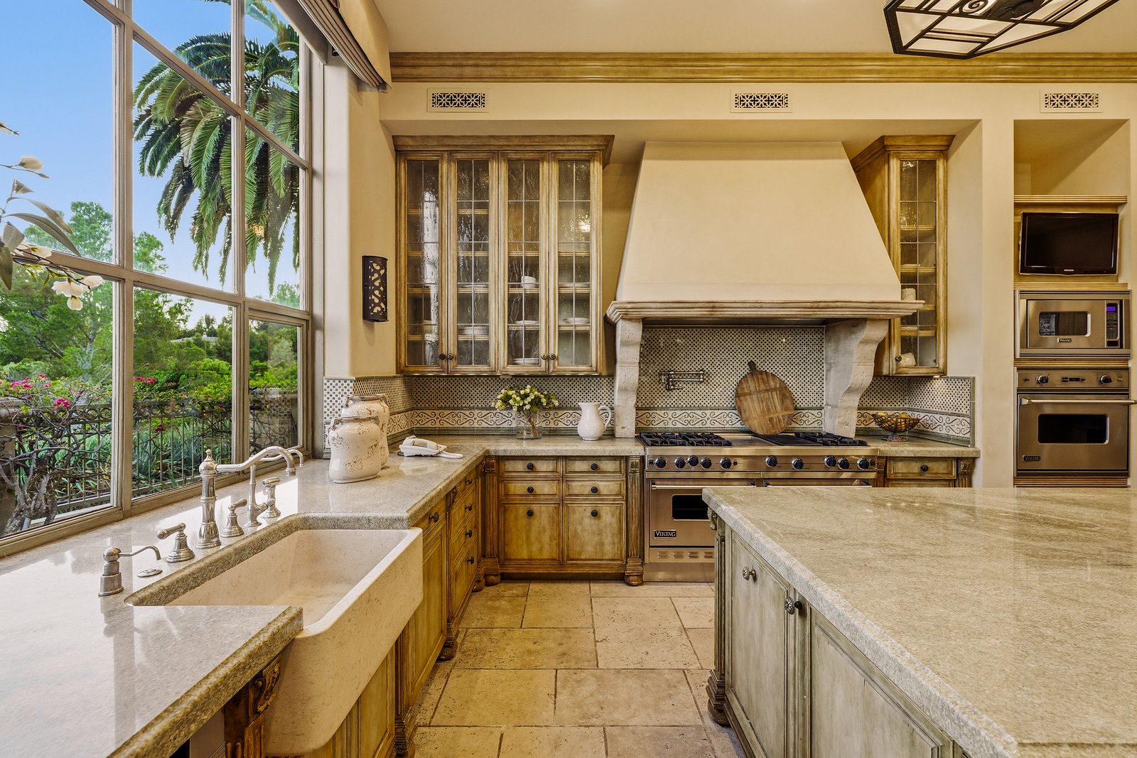 A stone range hood anchors the cooking area, framed by glass-front display cabinets and a professional-grade Viking range. 