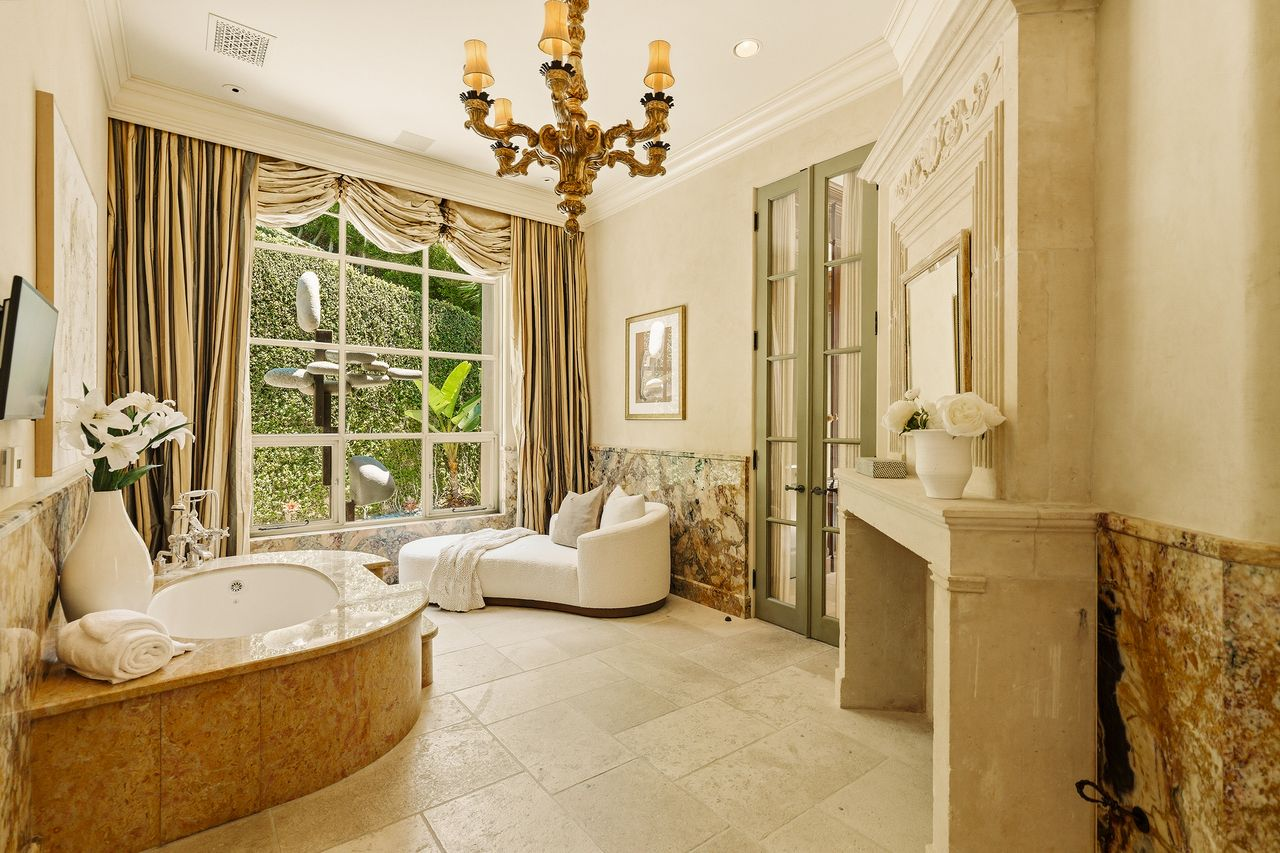 Paired with this closet is a bathroom featuring a soaking tub beneath a large picture window, a carved stone fireplace, and marble finishes.