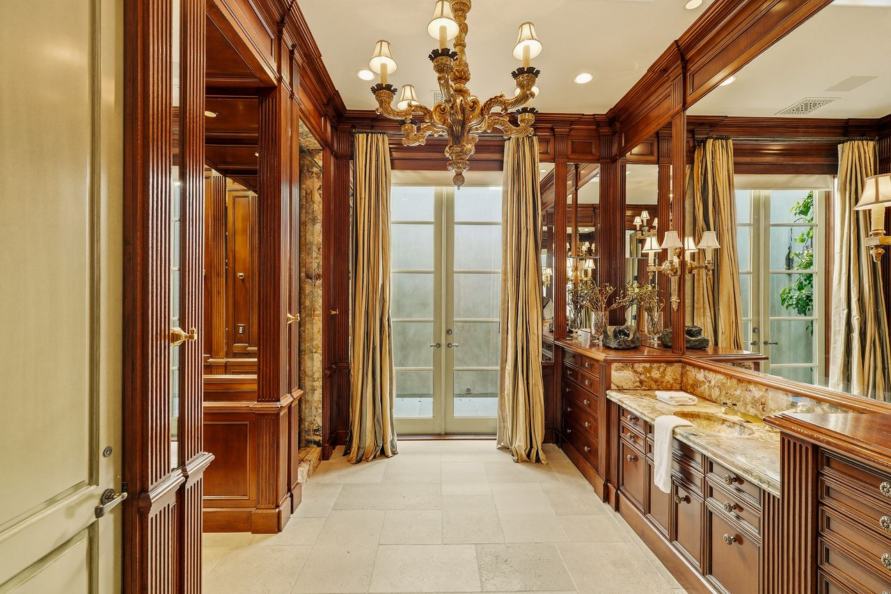 The adjoining bathroom continues the same rich wood detailing with marble countertops, custom vanities, and a walk-in shower.