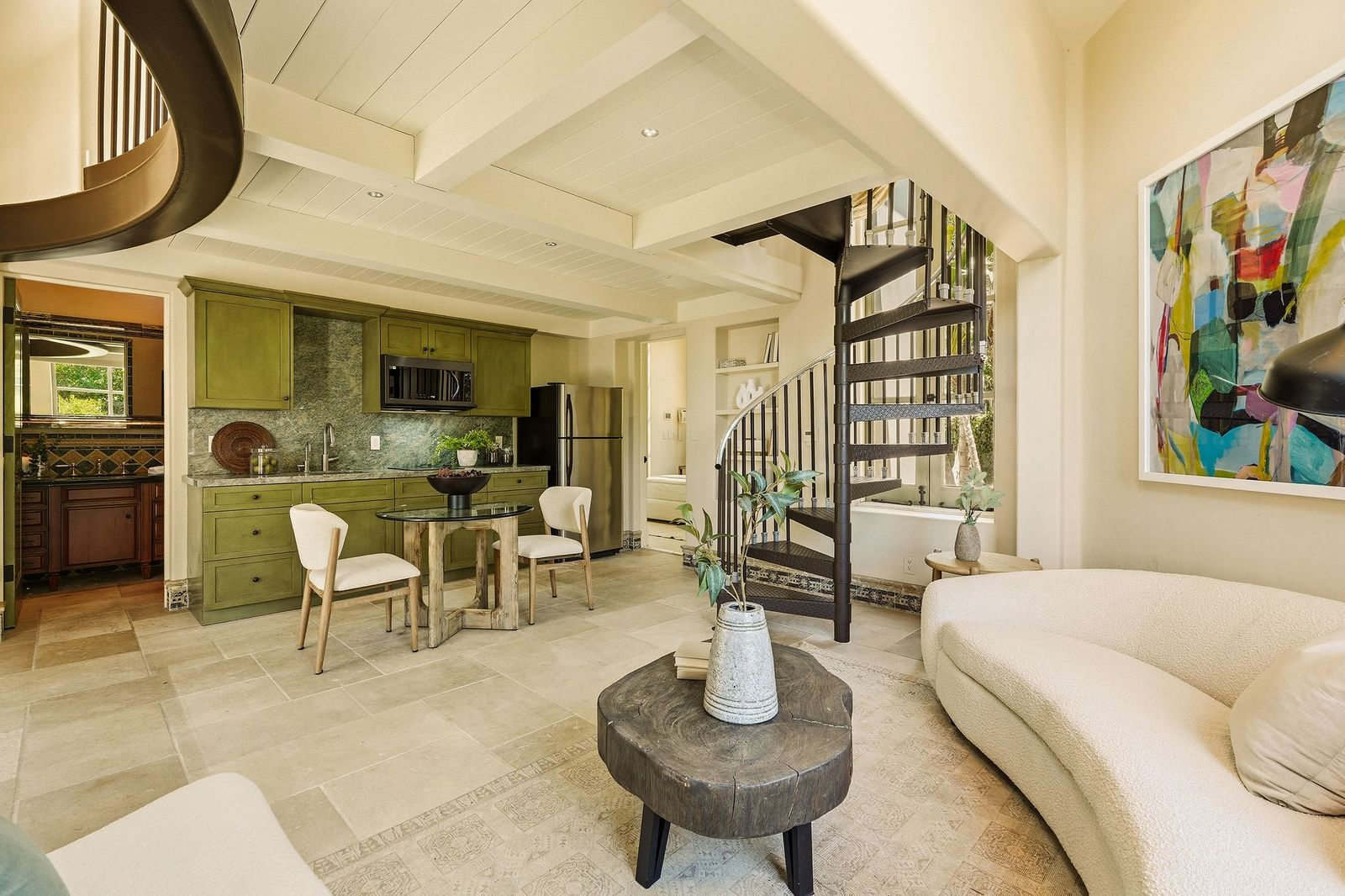The detached guest house begins with an open-concept living area that combines a lounge, kitchenette, and dining nook beneath a beamed ceiling. 