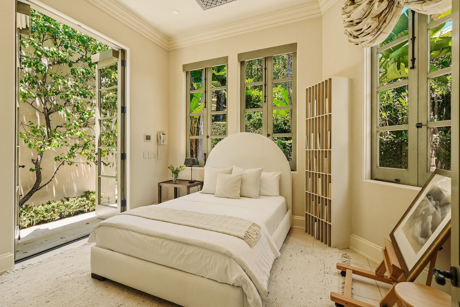 On the bottom floor, the guest bedroom continues the bright, airy feel with tall windows on three sides and French doors that open to the landscaped grounds.