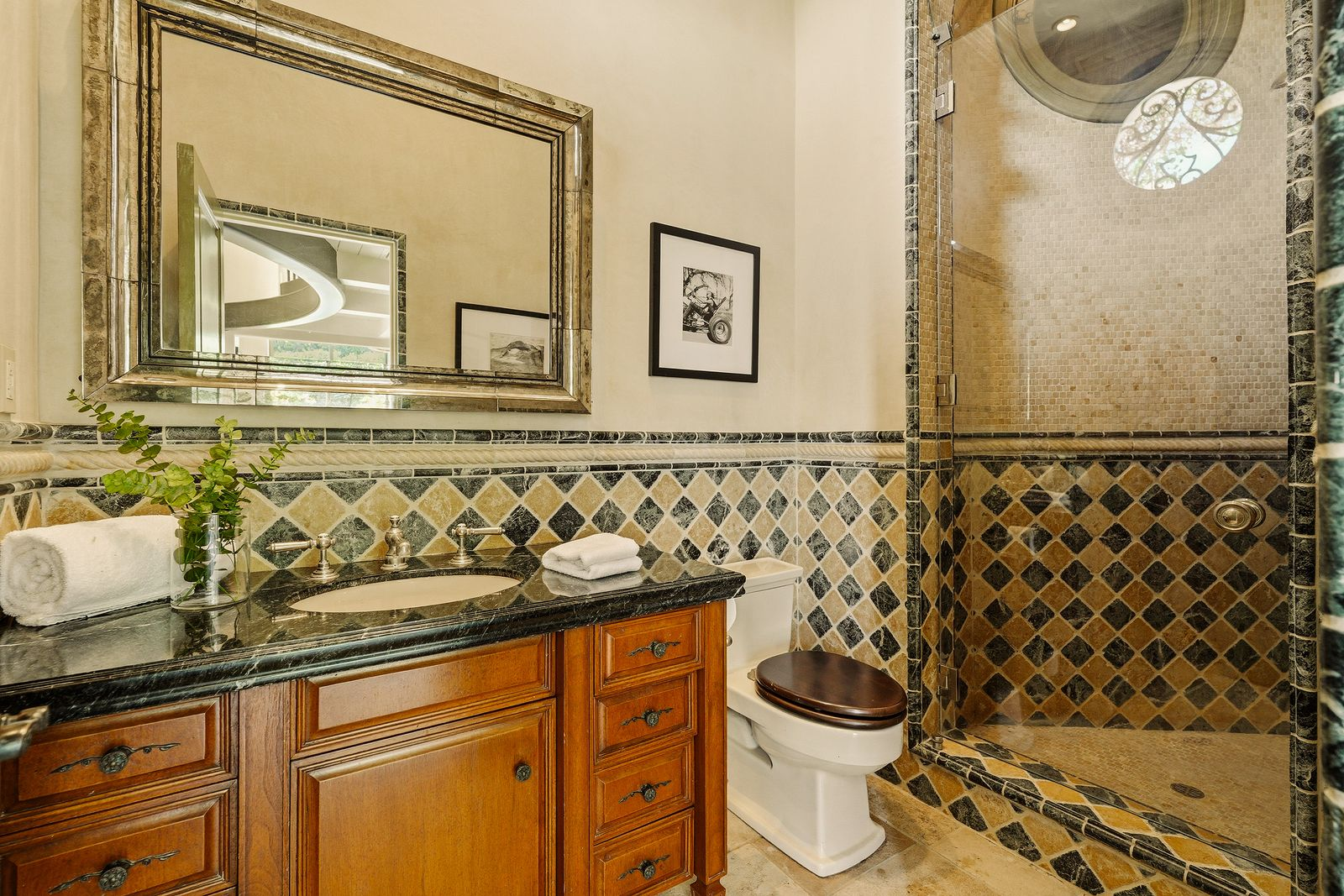 Finished with rich wood cabinetry and patterned stone tile, the guest bathroom includes a granite-topped vanity and a walk-in shower enclosed in glass.