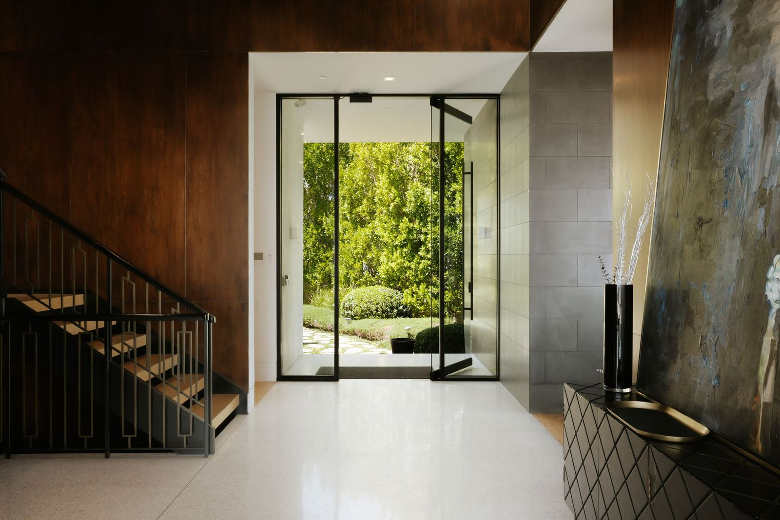 The home's dramatic double-height foyer immediately establishes its contemporary character with crisp terrazzo floors, floor-to-ceiling walnut millwork, and oversized pivoting glass doors.