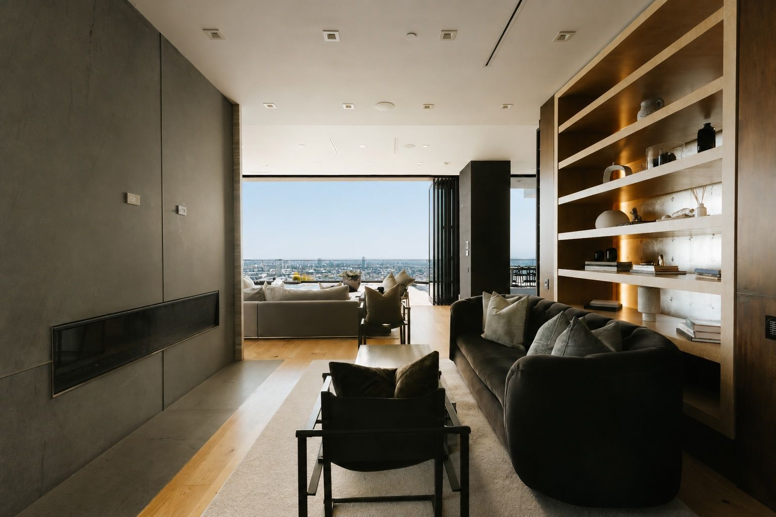 A sleek linear fireplace is set into a charcoal stone accent wall opposite illuminated walnut shelving and a low-profile couch.