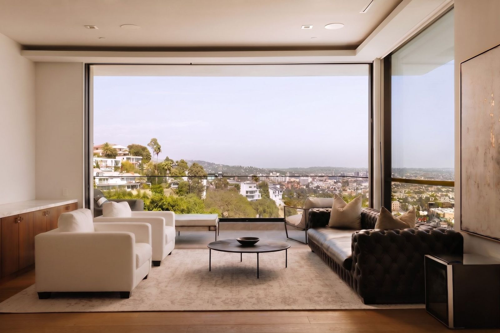 A sitting area featuring a pair of plush white chairs and a tufted leather sofa placed in front of an entire wall that slides open to a secluded terrace.